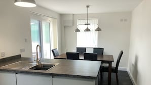 A modern kitchen with a central island, a dining area with a table and chairs, and a large window providing natural light. - Great property for exploring the Forest of Dean and surrounding areas. (Mile End, near Coleford)