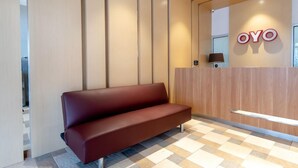 A reception area with a wooden reception desk, a red bench, and a wall-mounted sign that reads 'OYO'. - OYO 3159 Festive Inn (Medan)