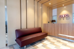 A reception area with a wooden reception desk, a red bench, and a wall-mounted sign that reads 'OYO'. - OYO 3159 Festive Inn (Medan)