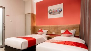 A hotel room with two beds, a wooden headboard, a painting on the wall, and a door with a sign. - OYO 3159 Festive Inn (Medan)