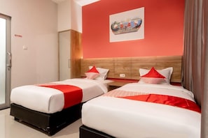A hotel room with two beds, a wooden headboard, a painting on the wall, and a door with a sign. - OYO 3159 Festive Inn (Medan)