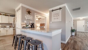 A modern kitchen with a central island, bar stools, and a ceiling fan. - Sweet Escape Homes: 3000sf Rustic Modern Home - Center of Dallas & FW (Grand Prairie)