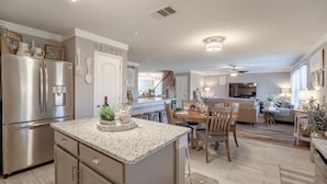 A modern kitchen with a large island, stainless steel appliances, and a dining area with wooden furniture. - Sweet Escape Homes: 3000sf Rustic Modern Home - Center of Dallas & FW (Grand Prairie)