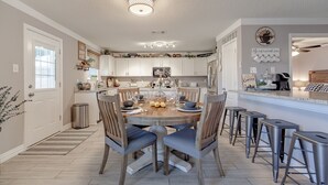A modern kitchen with a central island, bar stools, and a dining table set for six. - Sweet Escape Homes: 3000sf Rustic Modern Home - Center of Dallas & FW (Grand Prairie)