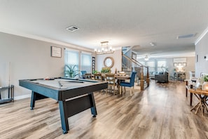 A spacious living area with a pool table, dining table, and a staircase leading to another level.