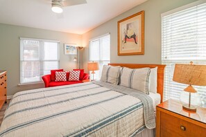 A bedroom with a large bed, a red sofa, two lamps, and a framed picture on the wall.
