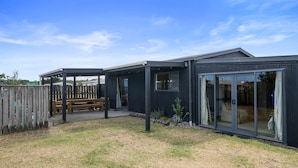 Une maison moderne dotée d’un patio couvert, d’une terrasse en bois et d’un jardin clôturé.