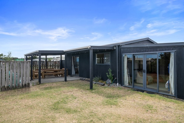 Een modern huis met een overdekte patio, een houten terras en een omheinde achtertuin.