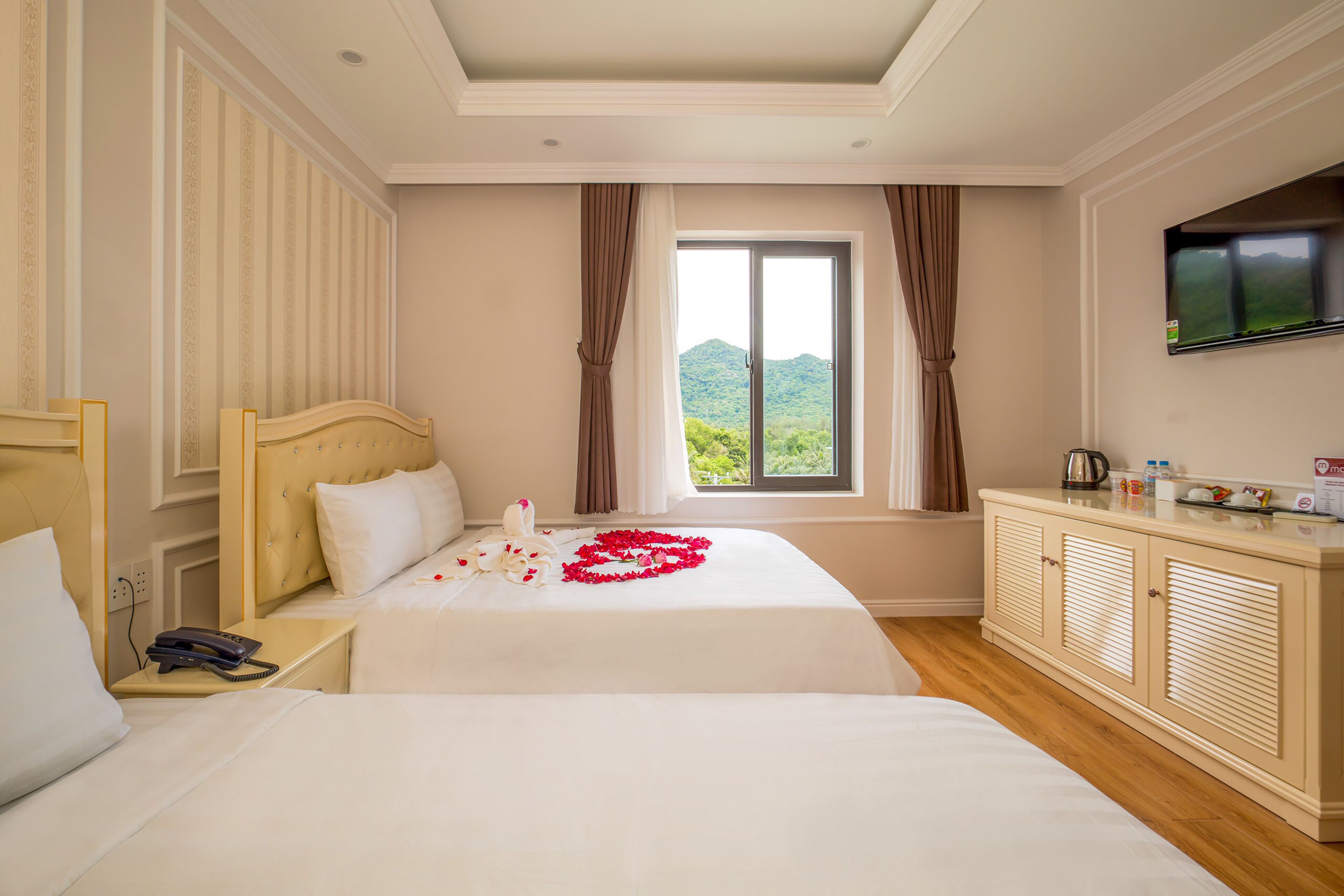 Habitación de hotel con dos camas, un televisor montado en la pared y una ventana con cortinas.
