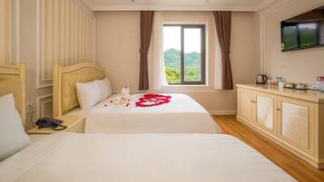 Habitación de hotel con dos camas, un televisor montado en la pared y una ventana con cortinas.