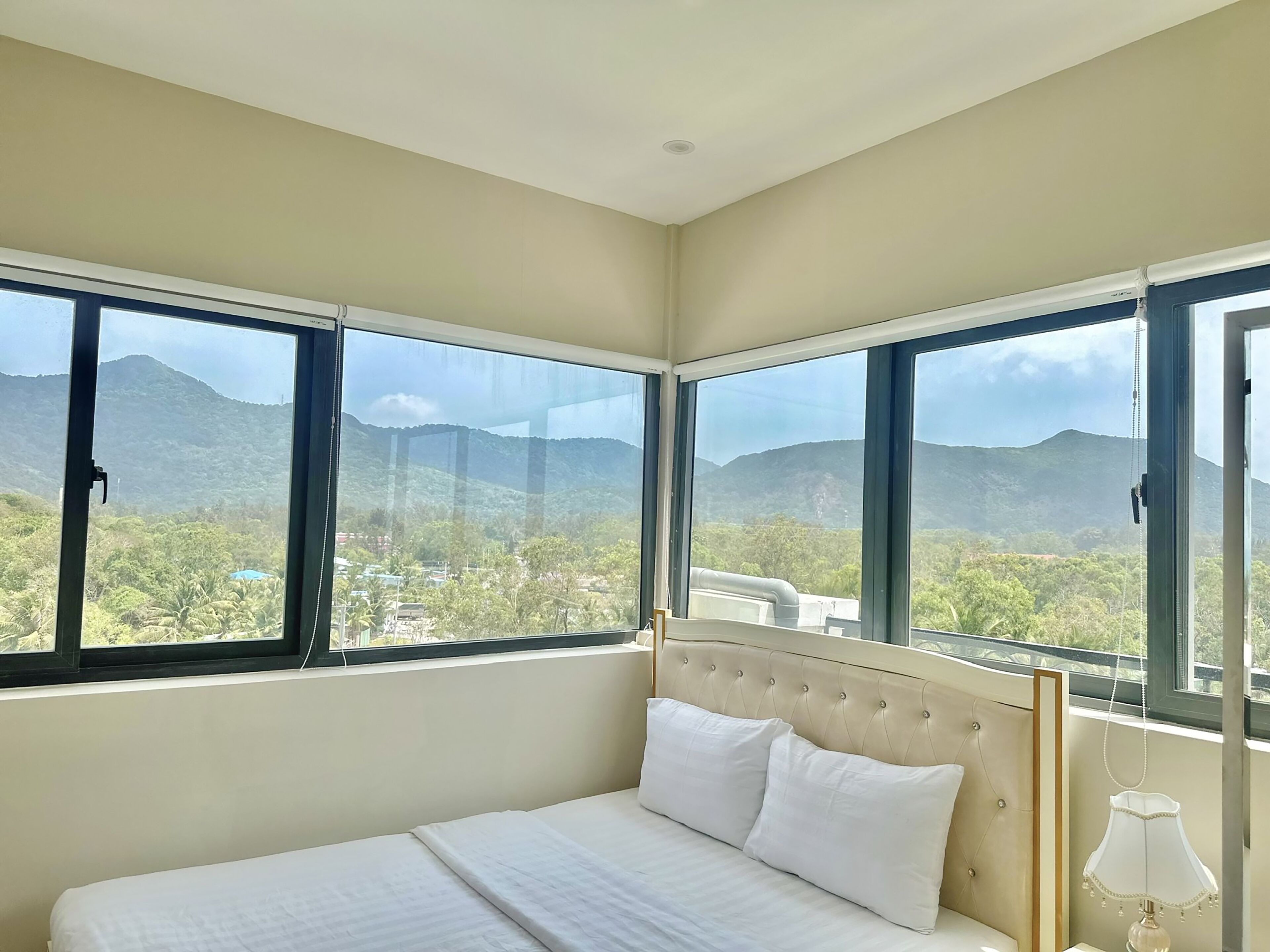 A bedroom with a large bed, two windows, and a view of mountains.