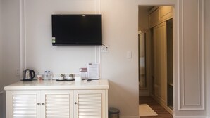 Habitación de hotel con televisor de pantalla plana montado en la pared, minibar con bebidas y aperitivos, un cubo de basura y una puerta que da al baño.