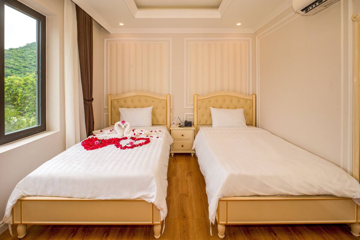 A double room with two beds, a nightstand, and a window with curtains.