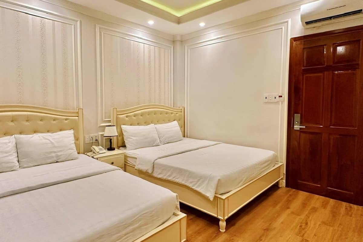 A hotel room with three beds, a wooden floor, and a wooden door.