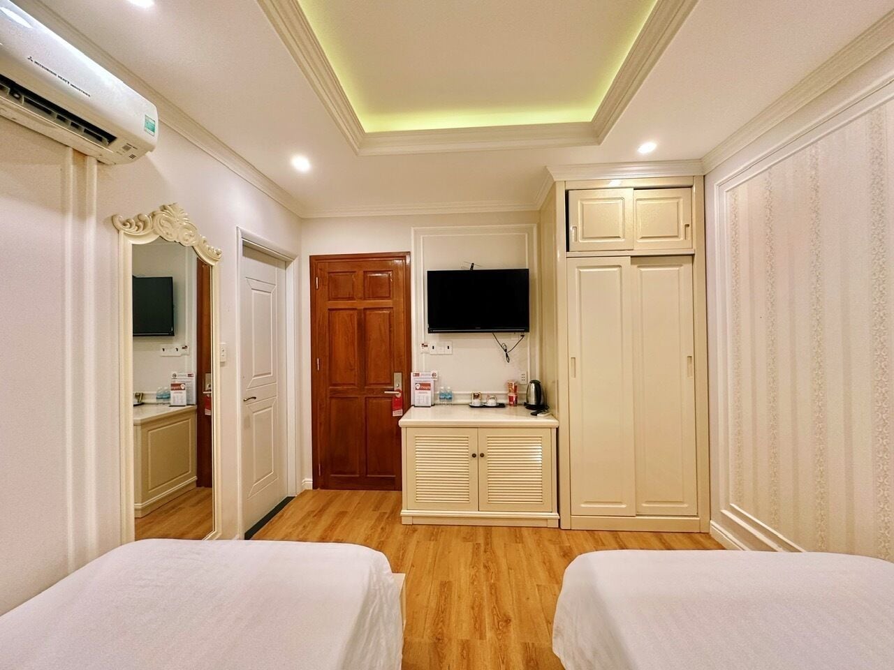 Habitació d'hotel amb dos llits, televisió, armari i una cuineta petita.