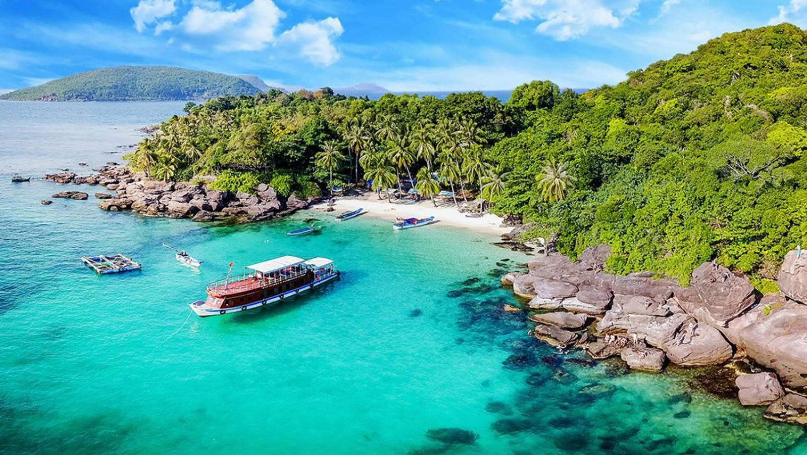 Una zona costera con aguas turquesas cristalinas, barcos y una costa rocosa con abundante vegetación.