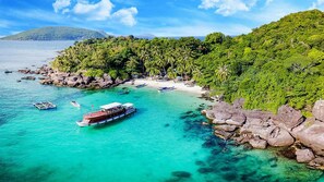 A coastal area with clear turquoise waters, boats, and a rocky shoreline with dense greenery. - Maya Hotel 2 (Ho Chi Minh City)