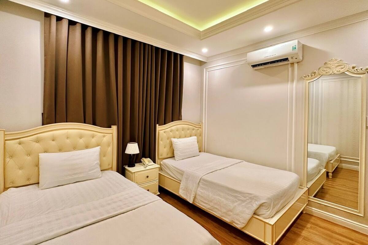 A hotel room with two beds, a nightstand, a lamp, an air conditioning unit, and a mirror.