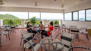 Una terraza con sillas y mesas de mimbre, vistas a colinas verdes y cielo despejado.