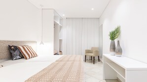 Ein modernes Schlafzimmer mit einem großen Bett, einem Nachttisch, einem Sessel und einem Schreibtisch mit zwei Vasen.