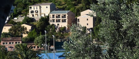 A hotel with a balcony on the second floor, surrounded by trees and other buildings.
