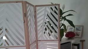 Huoneessa on punainen sohva, koristeellinen väliseinä, jossa on geometrisia kuvioita, kirjahylly täynnä kirjoja ja ruukussa oleva kasvi.