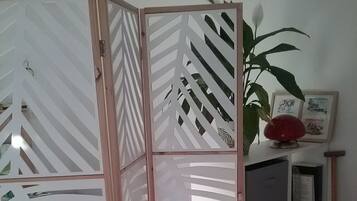 Een kamer met een rode bank, een decoratieve scheidingswand met geometrische patronen, een boekenplank vol boeken en een potplant.