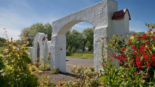 Un arco de piedra con un muro blanco y un pequeño edificio con techo rojo.
