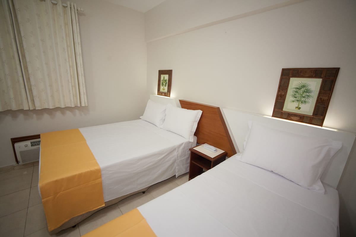 A hotel room with two single beds, a bedside table with a lamp, and a wall-mounted picture frame.