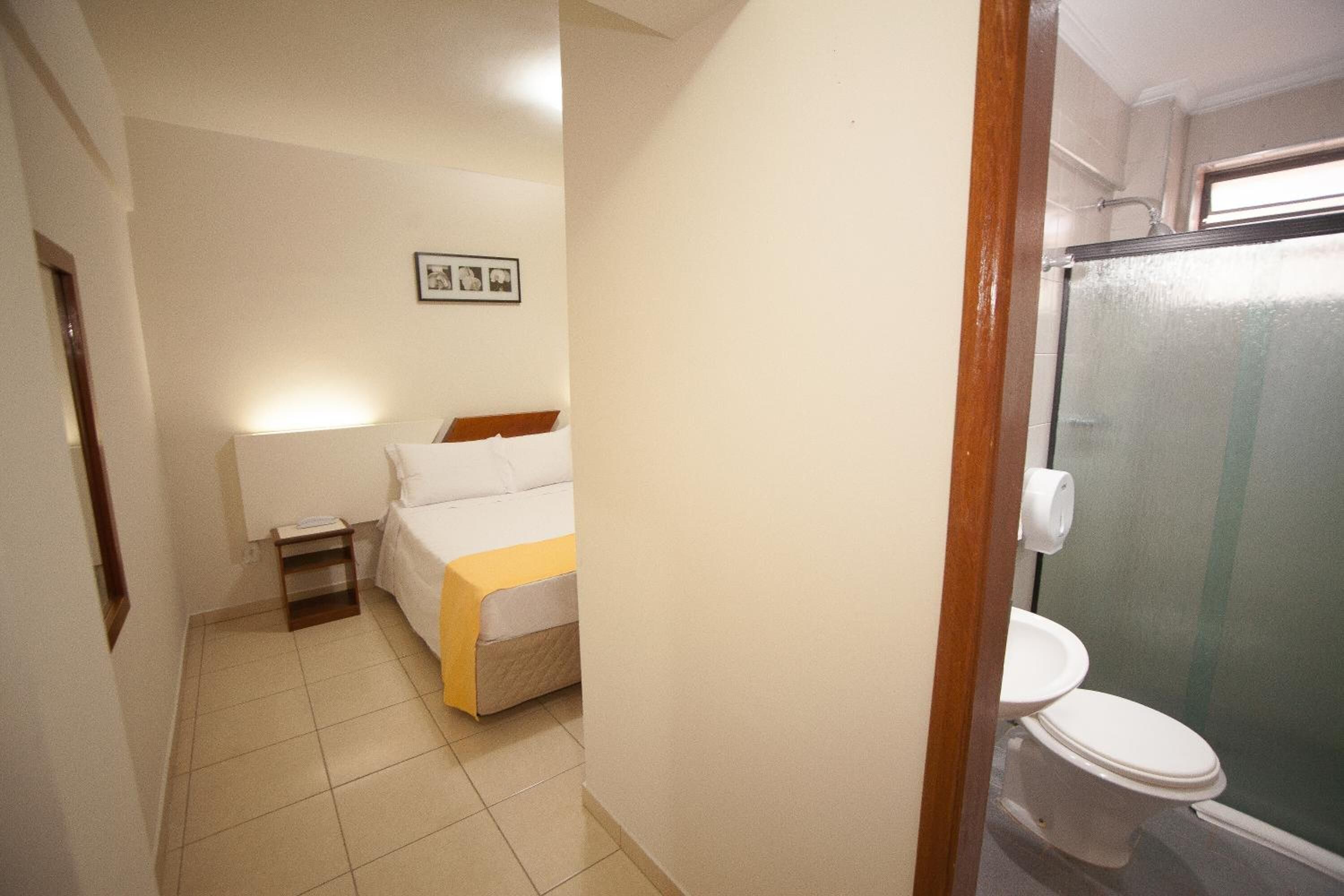A hotel room with a bed, bedside table, and a bathroom with a toilet and shower.