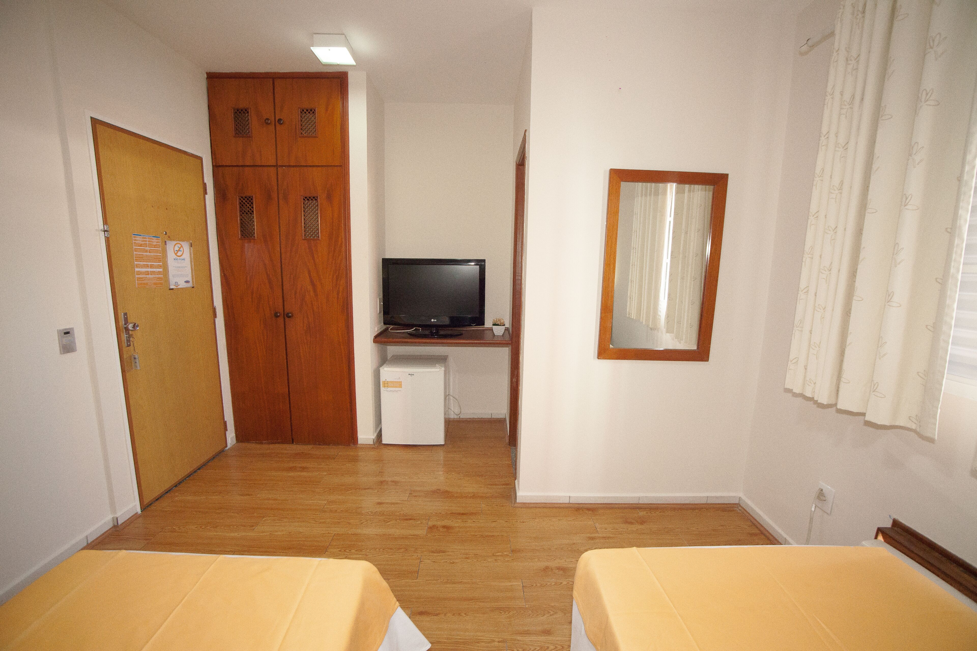 Una habitación con suelo de madera, un escritorio con computadora, un televisor y dos camas con ropa de cama amarilla.