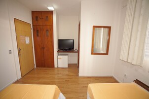 Una habitación con suelo de madera, un escritorio con computadora, un televisor y dos camas con ropa de cama amarilla.