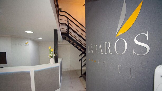 Vastaanottotiski, jossa on kyltti, jossa lukee ”LAPAROS HOTEL”, ja portaikko, joka johtaa ylempään kerrokseen.