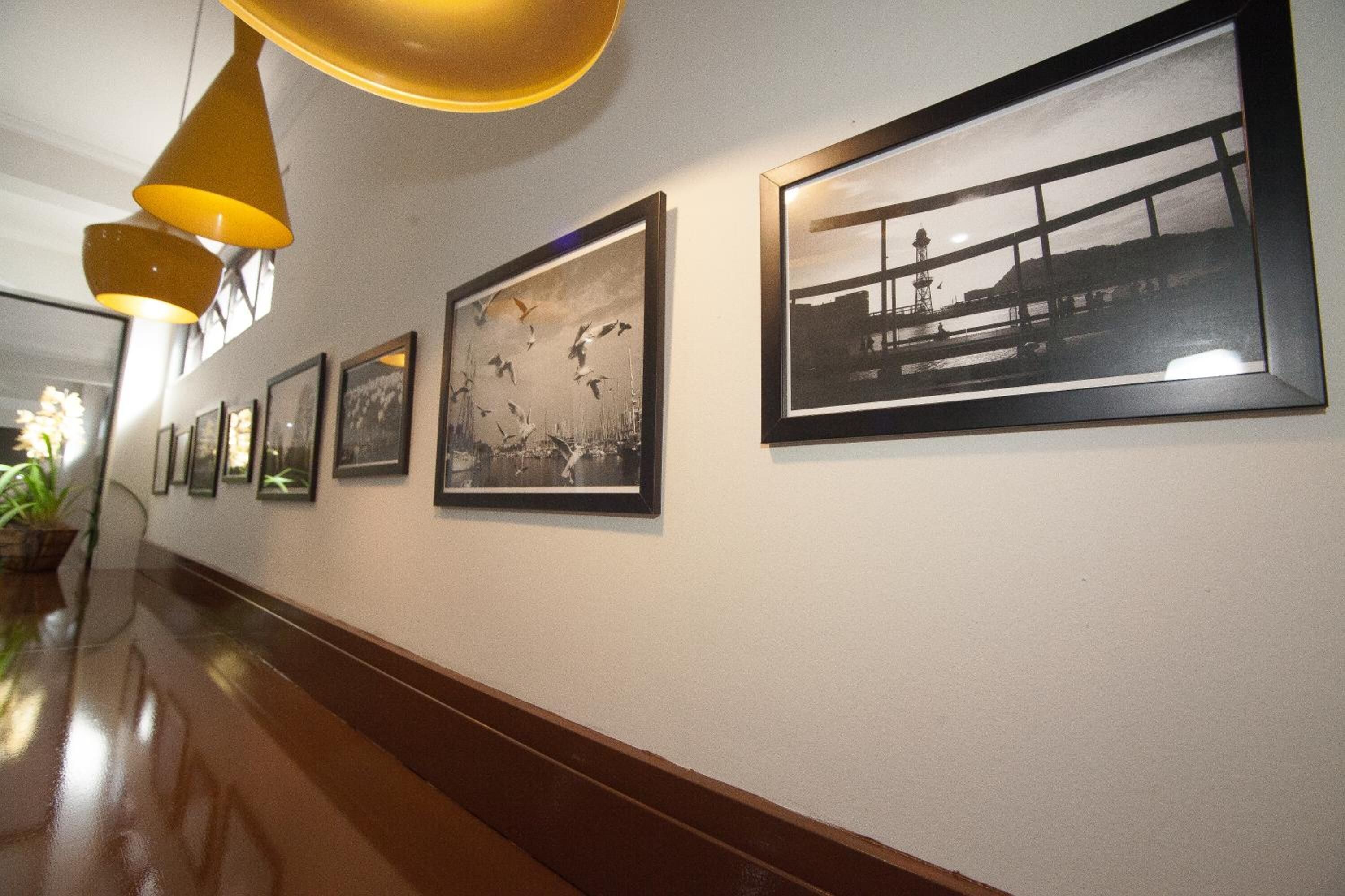 Een gang met ingelijste foto’s aan de muur, een glanzende houten vloer en hanglampen.