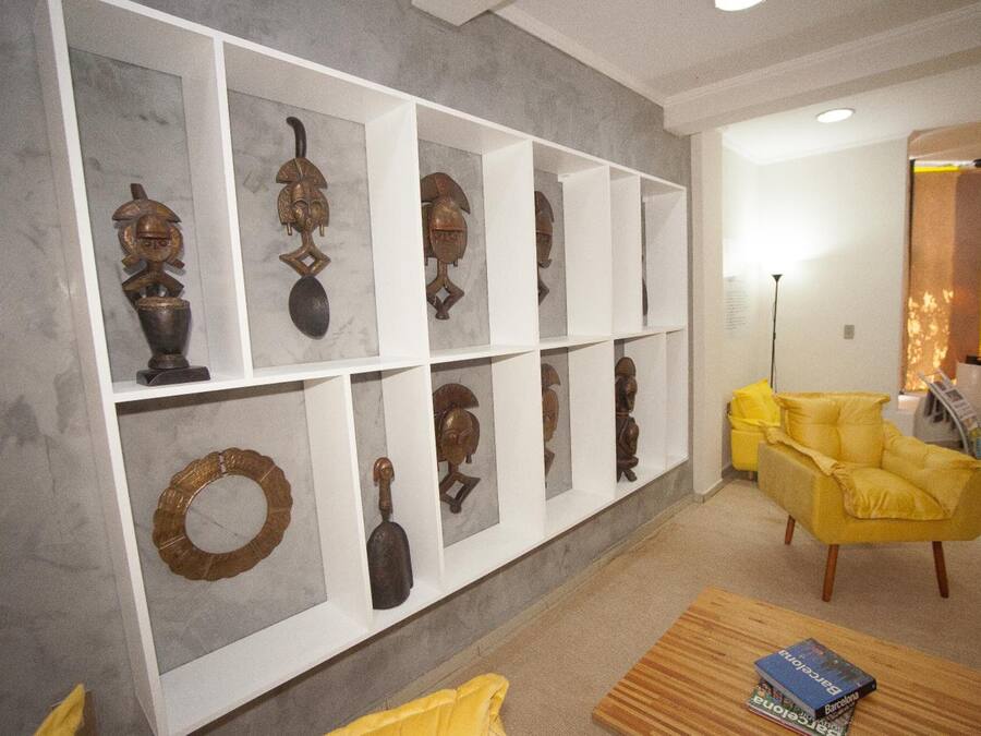 A room with a white wall displaying various wooden sculptures and a yellow armchair.