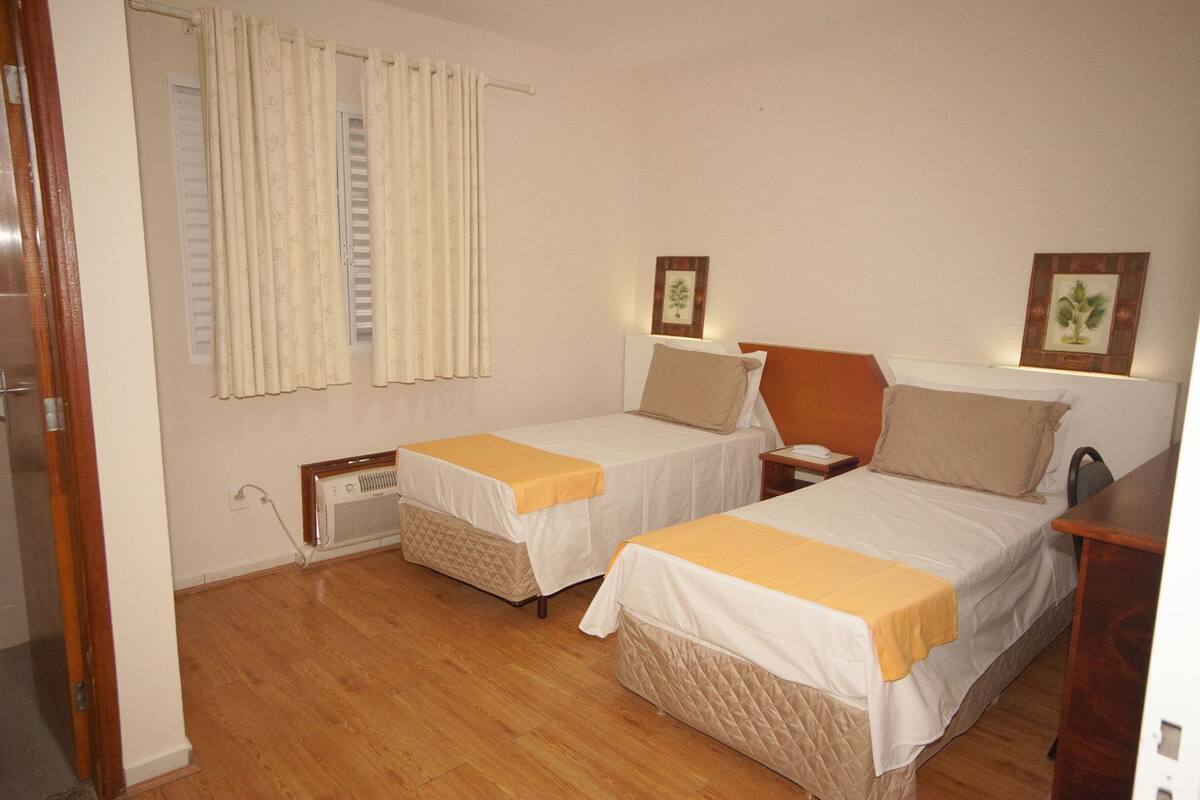 A room with two beds, a window with curtains, a radiator, and a wall-mounted picture.