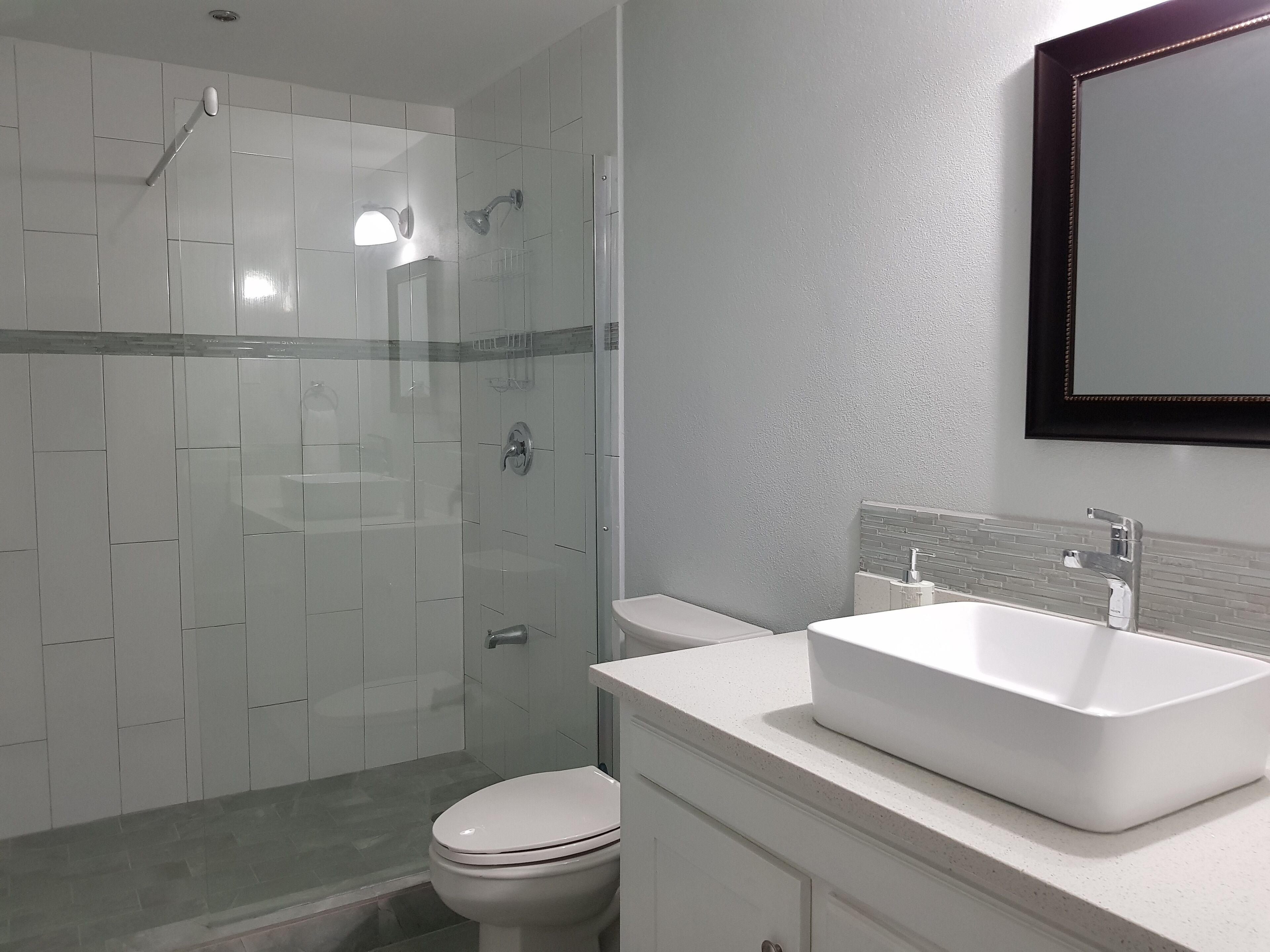 A modern bathroom with a glass-enclosed shower, a white toilet, and a large sink with a mirror above it.