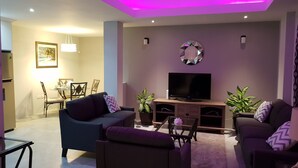 Ein modernes Wohnzimmer mit Flachbildfernseher, zwei Sofas, einem Essbereich mit Tisch und Stühlen sowie Wandkunst.