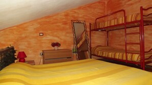 Une chambre avec un lit superposé, un matelas jaune, une commode en bois, une lampe rouge et un miroir.