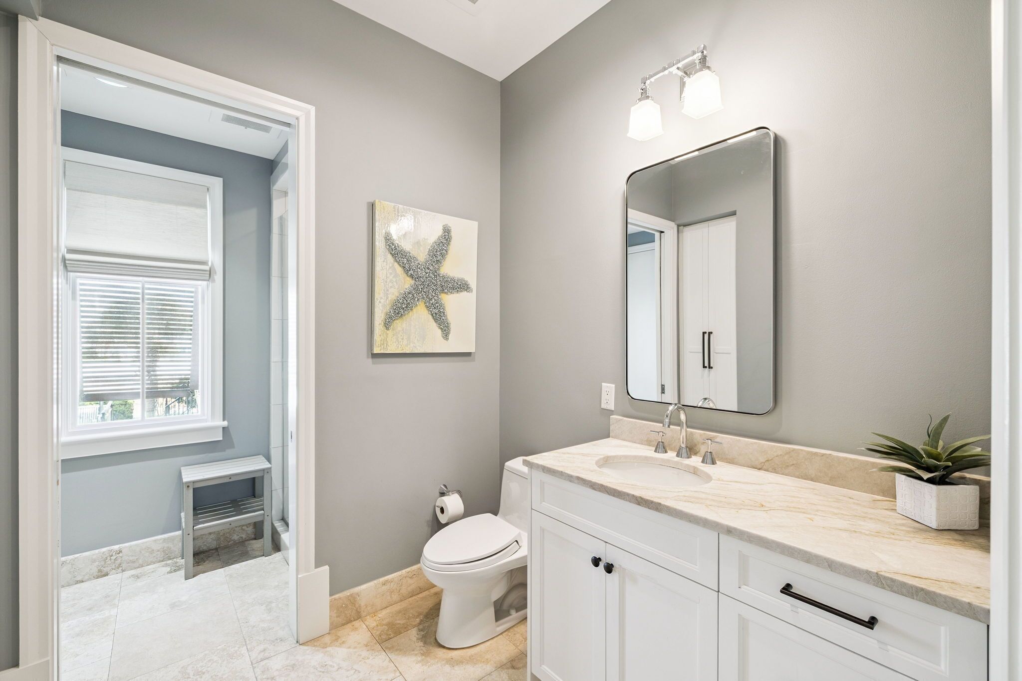 A bathroom with a white vanity, a large mirror, a starfish decoration, and a window with blinds.