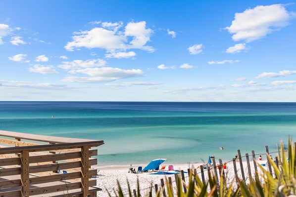 Relax on the beach with a clear ocean view from the deck, featuring comfortable seating and umbrellas.