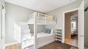 A bunk bed room with a white ladder, a small shelf, and a door leading to another room.