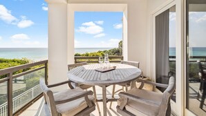 A round wooden table with four chairs, a glass pitcher, and a wine glass on a balcony overlooking the ocean. - Beachfront haven with chef’s kitchen, private garage, beach access, & 6 bikes! (Seagrove Beach)
