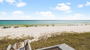 A beach with a wooden walkway leading to the shore, a row of green umbrellas, and a clear view of the ocean.