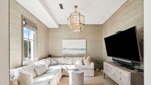 A modern living room with a sectional sofa, a flat-screen TV, a decorative light fixture, and a large window.