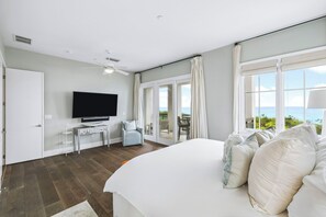 A hotel room with a large bed, a flat-screen TV, a desk with a computer, a chair, and a balcony with a view of the ocean. - Beachfront haven with chef’s kitchen, private garage, beach access, & 6 bikes! (Seagrove Beach)
