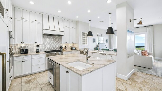 A modern kitchen with white cabinetry, a central island, and a dining area with a view. - Beachfront haven with chef’s kitchen, private garage, beach access, & 6 bikes! (Seagrove Beach)