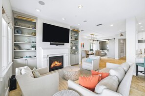 A modern living room with a fireplace, a flat-screen TV, and a dining area with a table and chairs. - Beachfront haven with chef’s kitchen, private garage, beach access, & 6 bikes! (Seagrove Beach)