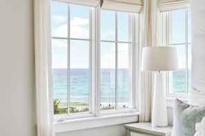 A room with a large window overlooking a beach, a bedside table, and a lamp. - Beachfront haven with chef’s kitchen, private garage, beach access, & 6 bikes! (Seagrove Beach)
