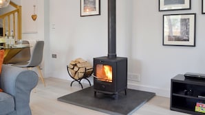 A living room with a black wood-burning stove, a dining table with chairs, and framed pictures on the wall. - 2 bedroom accommodation in Grosmont, near Abergavenny (Grosmont, near Abergavenny)